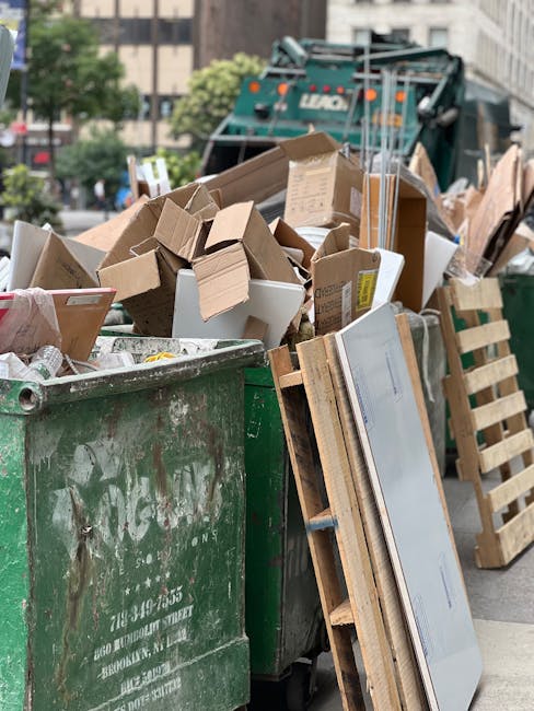 A collection of overflowing rubbish bins and scattered waste on a paved sidewalk in an urban area, visible in front of a commercial building with shuttered shops and a blue scaffold structure. The rub
